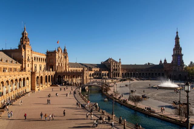 People walking in Plaza de España in Seville with the canal and bridges in view