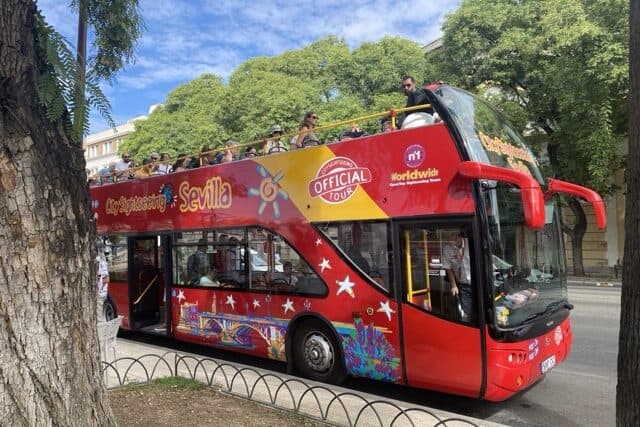 Red Seville hop-on hop-off sightseeing bus stopped along Paseo de Colón in Seville