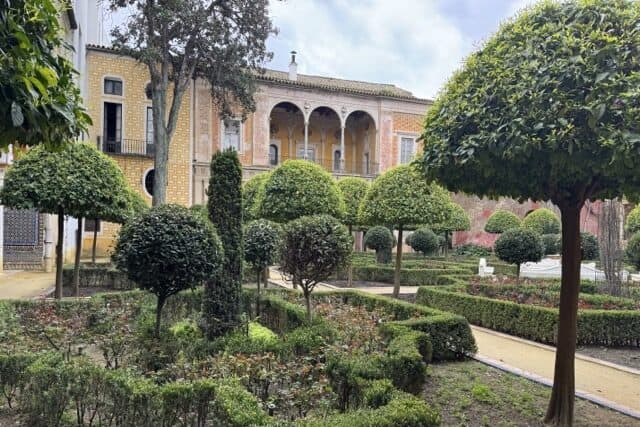 Garden courtyard at Casa de Pilatos in Seville with trees, plants and the palace facade in the background